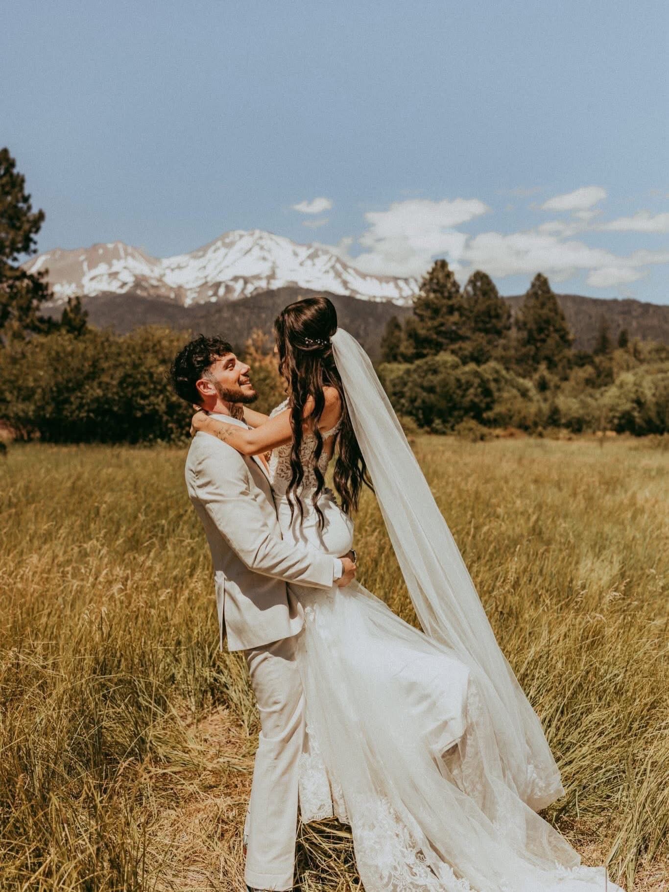 Evan lifting Sarah in a meadow with the snow-capped peaks of Mt. Shasta behind them